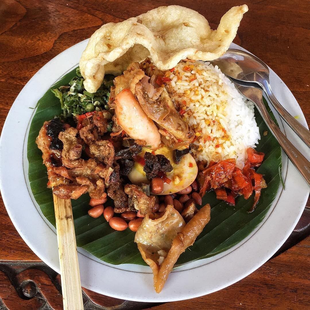 Nasi ayam campur on a banana leaf: rice, sate lilit, shredded chicken, egg, crispy skin, peanuts, sambal and a cracker