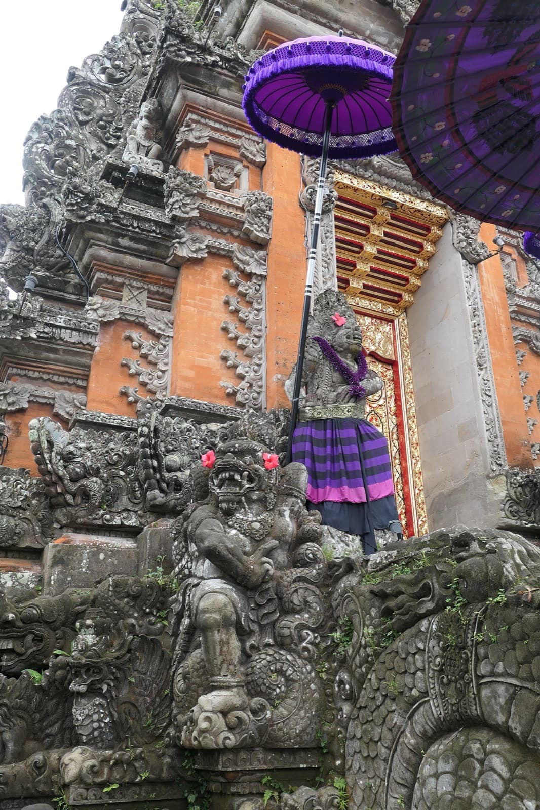 The Kori Agung gate with a guardian statue dressed in cloth and purple ceremonial umbrellas