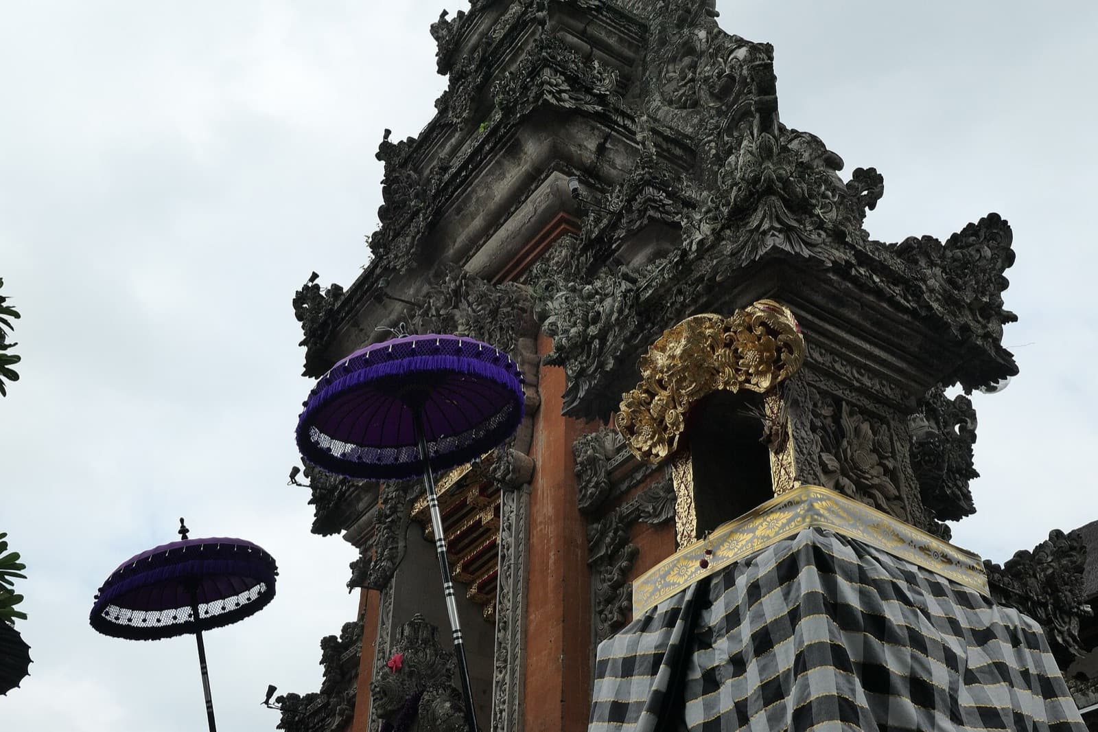 Carved shrine wrapped in checkered cloth next to purple umbrellas