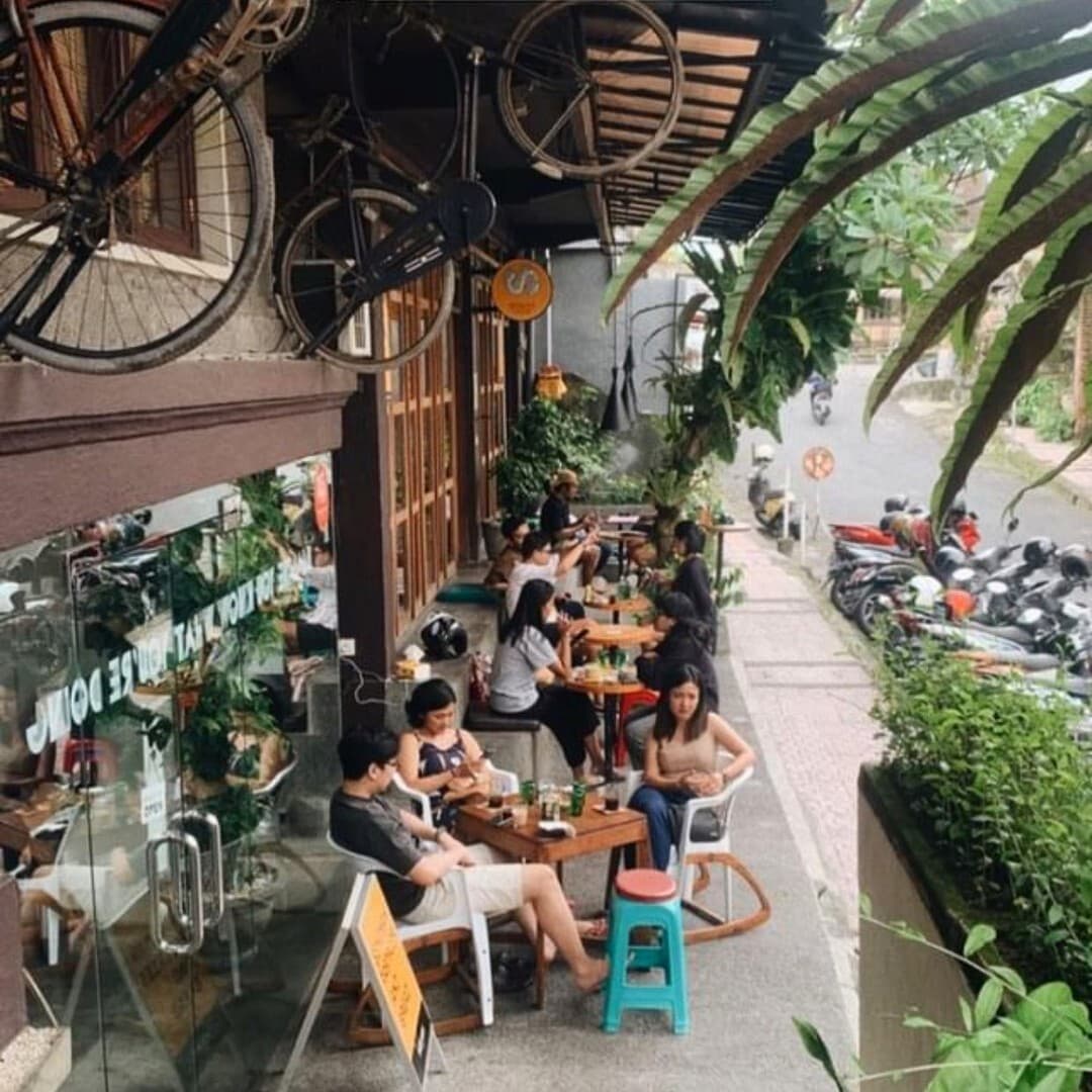 People at the tables on the pavement terrace, under old bicycles hanging from the eaves