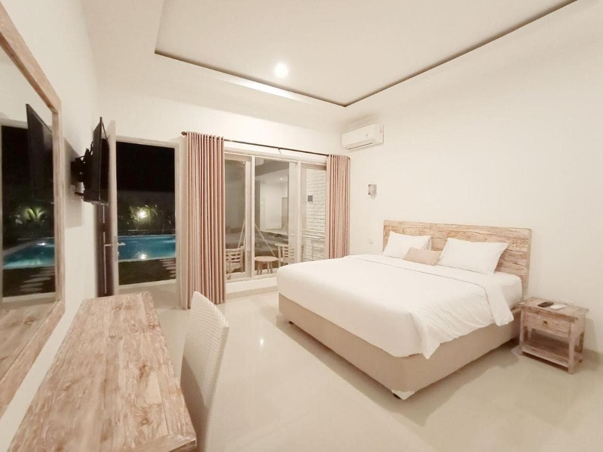 a white bedroom with a bed and a table at Berawa Dini Guesthouse in Canggu