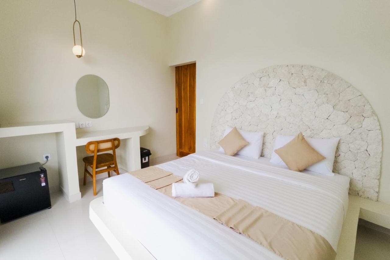 a bedroom with a large white bed and a chair at Kula Uluwatu in Uluwatu