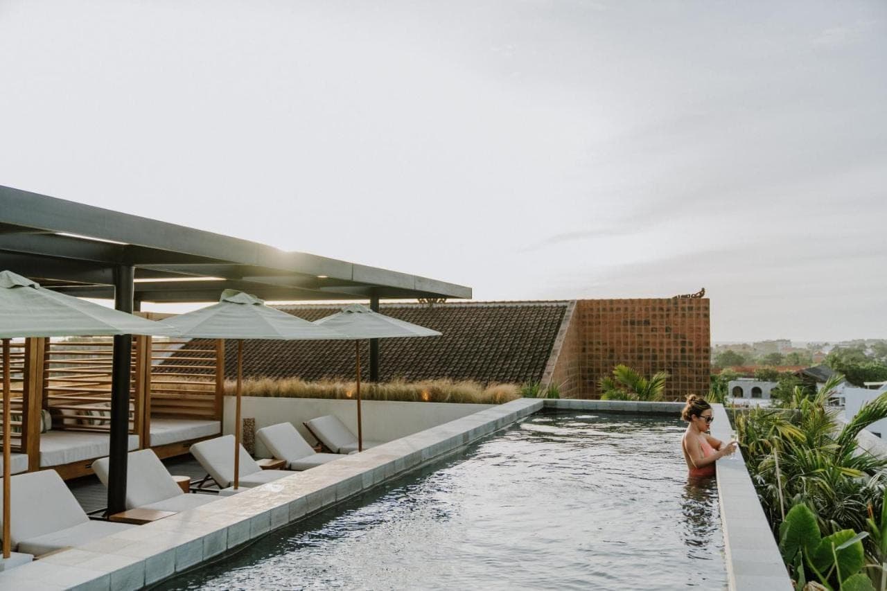 a woman standing in a swimming pool next to a building at The Komu Canggu Bali in Canggu