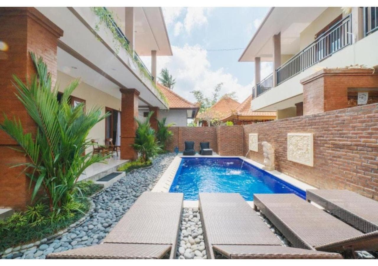 a swimming pool with chaise lounges next to a building at Komala Homestay in Canggu