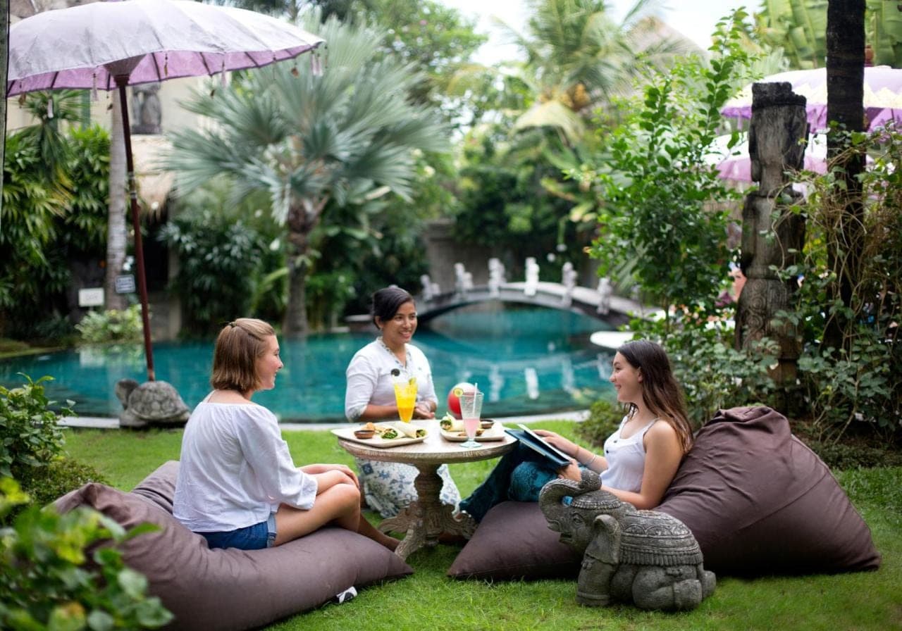 three people sitting around a table in the grass near a pool at Blue Karma Seminyak in Seminyak