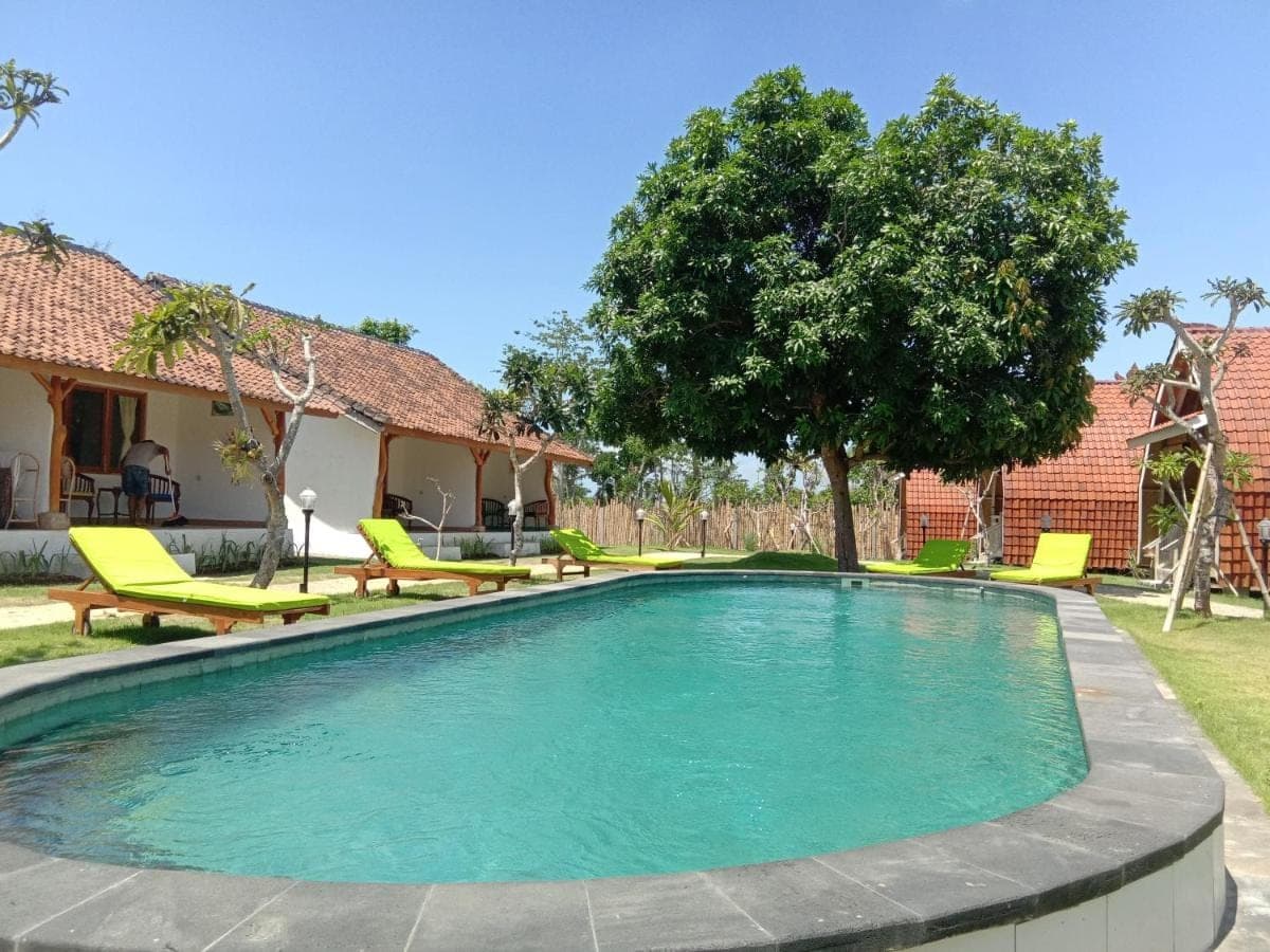 a swimming pool with green chairs and a house at La Cama Bali in Uluwatu