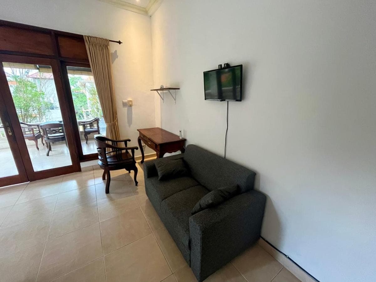 a living room with a couch and a tv on a wall at Permana Cottage Ubud in Ubud