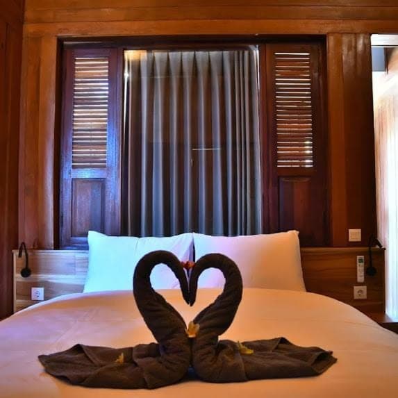 two swans are making a heart shape on a bed at Putra'Lebah Amed Guest House in Amed