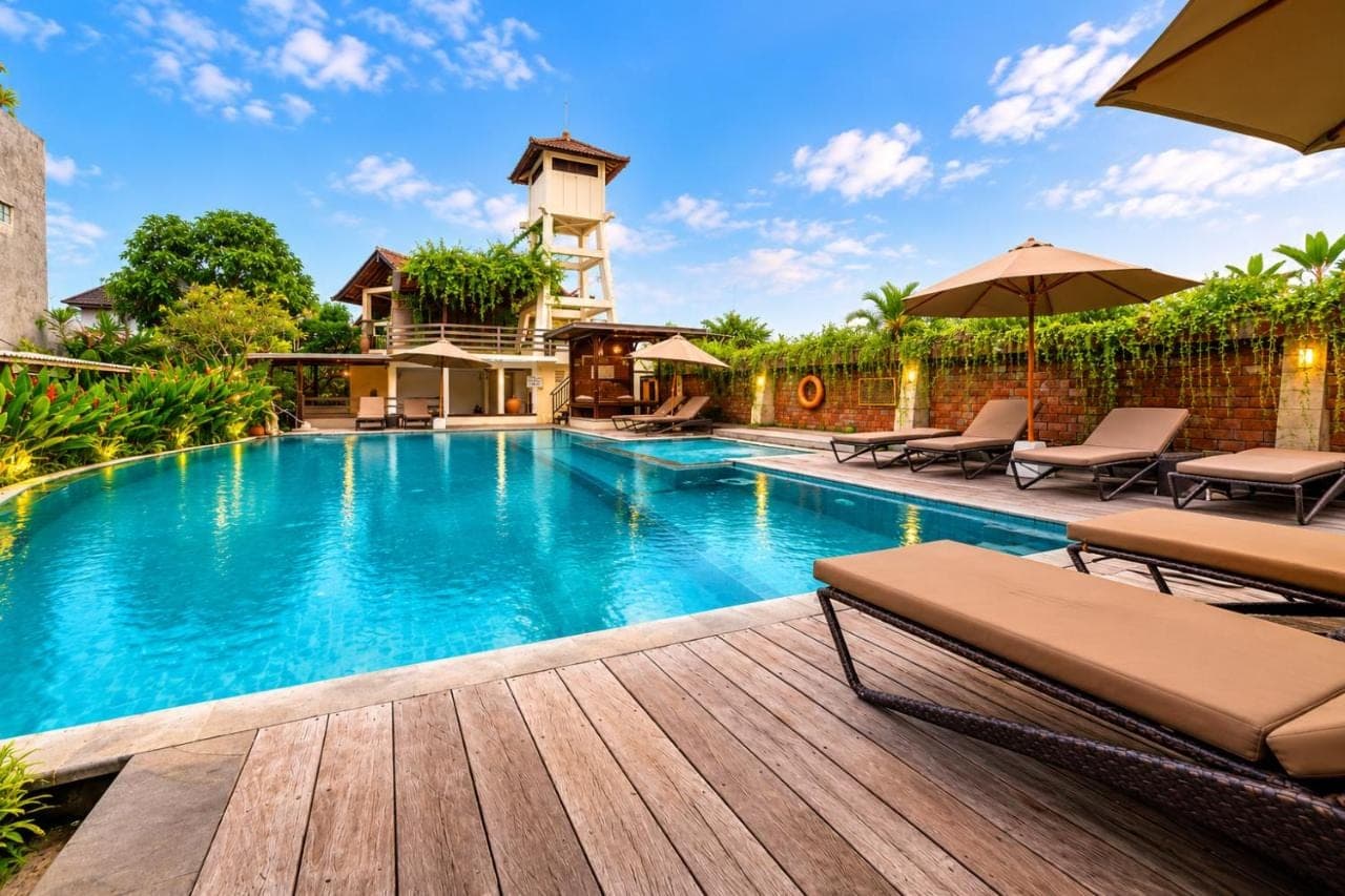 a swimming pool with a deck with chairs and umbrellas at Bali Ayu Hotel &amp; Villas 10 Minutes Walking Distance to the Beach in Seminyak