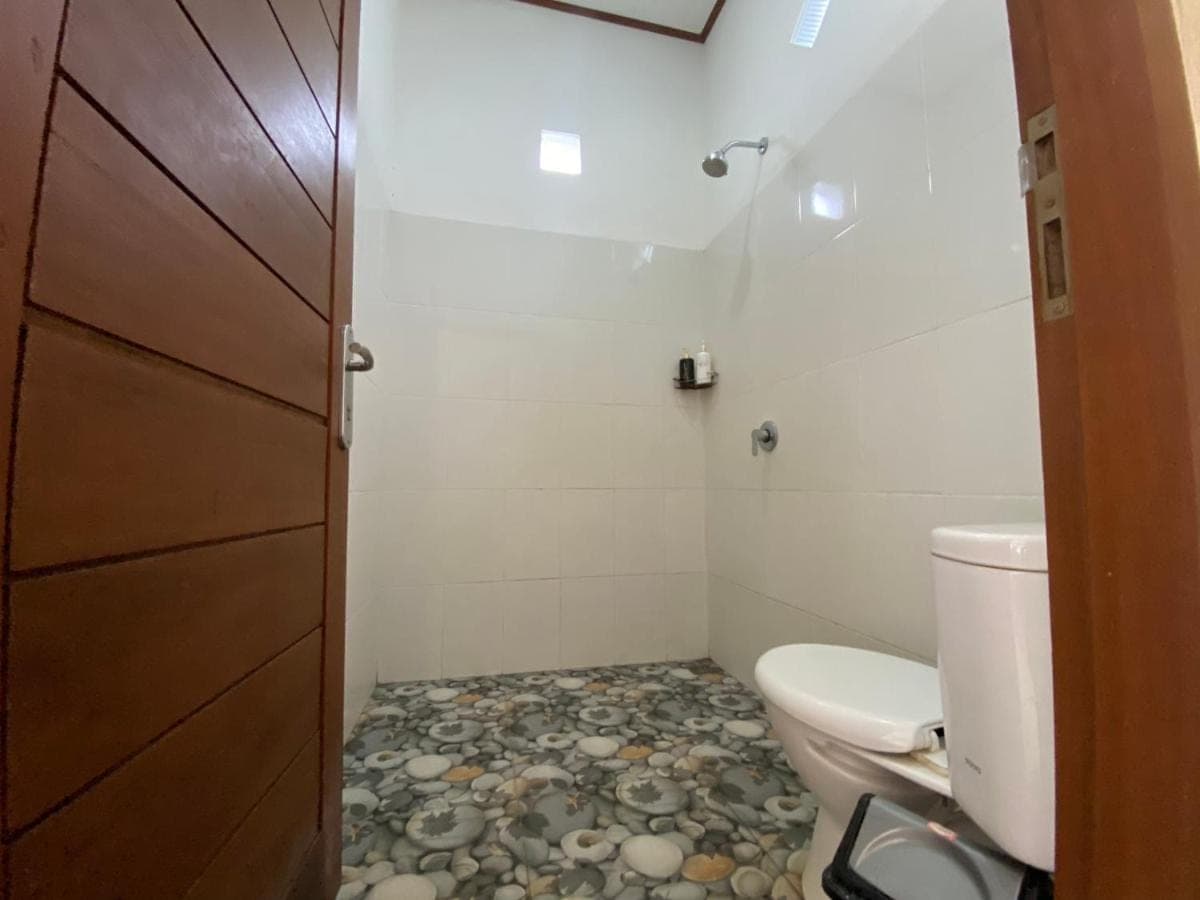 a bathroom with a toilet and a rock floor at Milla's Homestay in Sidemen