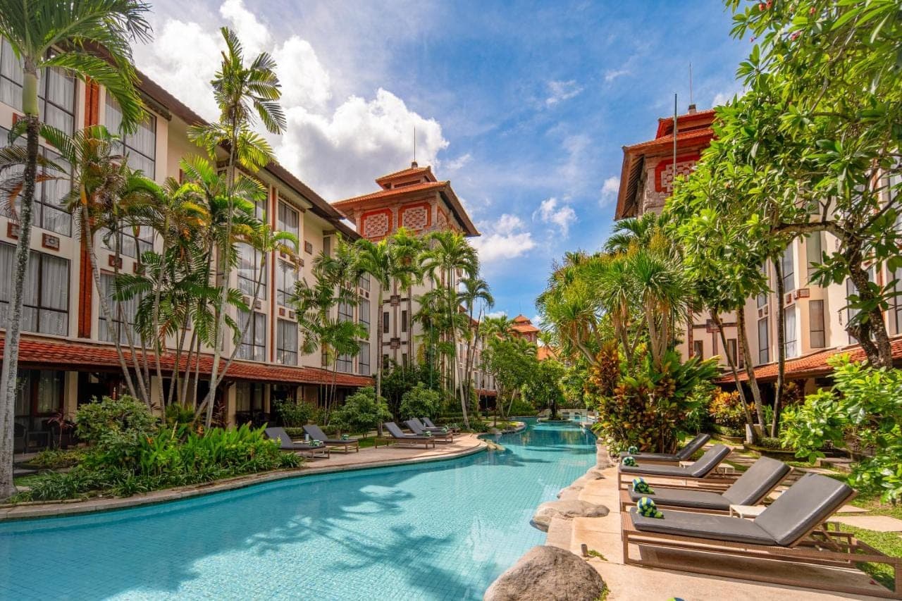 a resort swimming pool with chaise lounge chairs and palm trees at Prime Plaza Hotel Sanur \u2013 Bali in Sanur