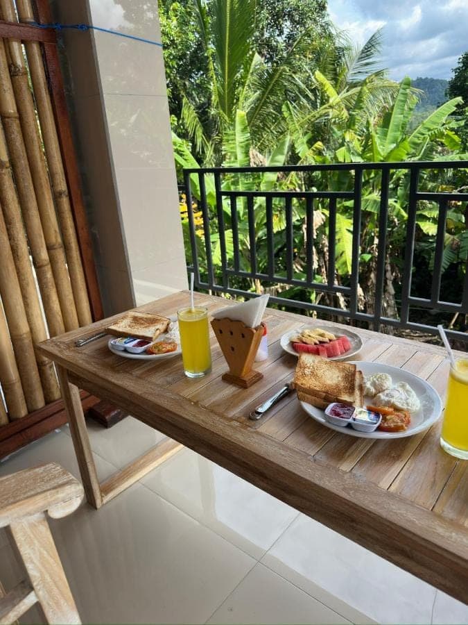a table with plates of food and drinks on a balcony at D'Kusuma House Sidemen in Sidemen