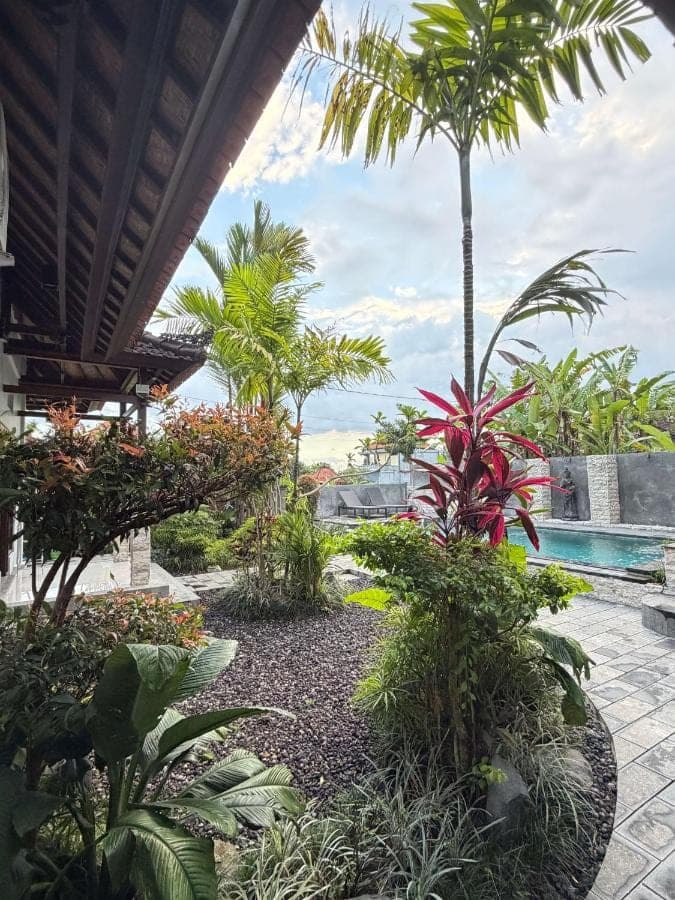 a garden with palm trees and a swimming pool at Anugrah Rice Field House in Ubud
