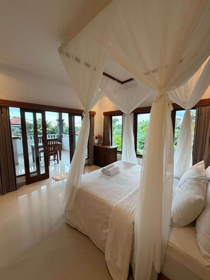 a bedroom with a white bed with a canopy at Anugrah Rice Field House in Ubud