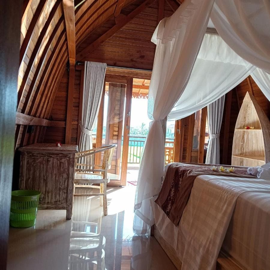 a bedroom with a canopy bed in a wooden house at Agung Inn Amed in Amed