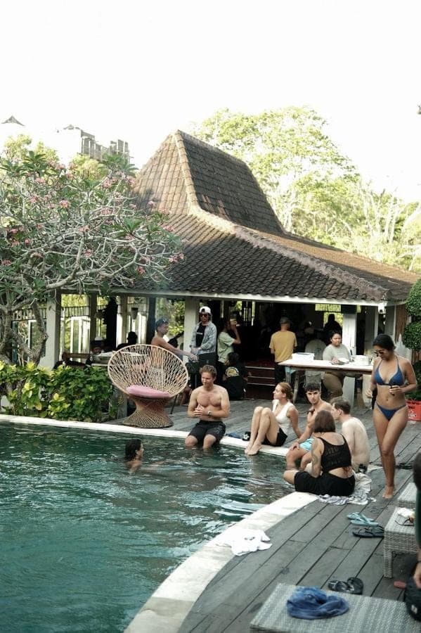 a group of people sitting around a swimming pool at One More Wave Surf House Uluwatu in Uluwatu