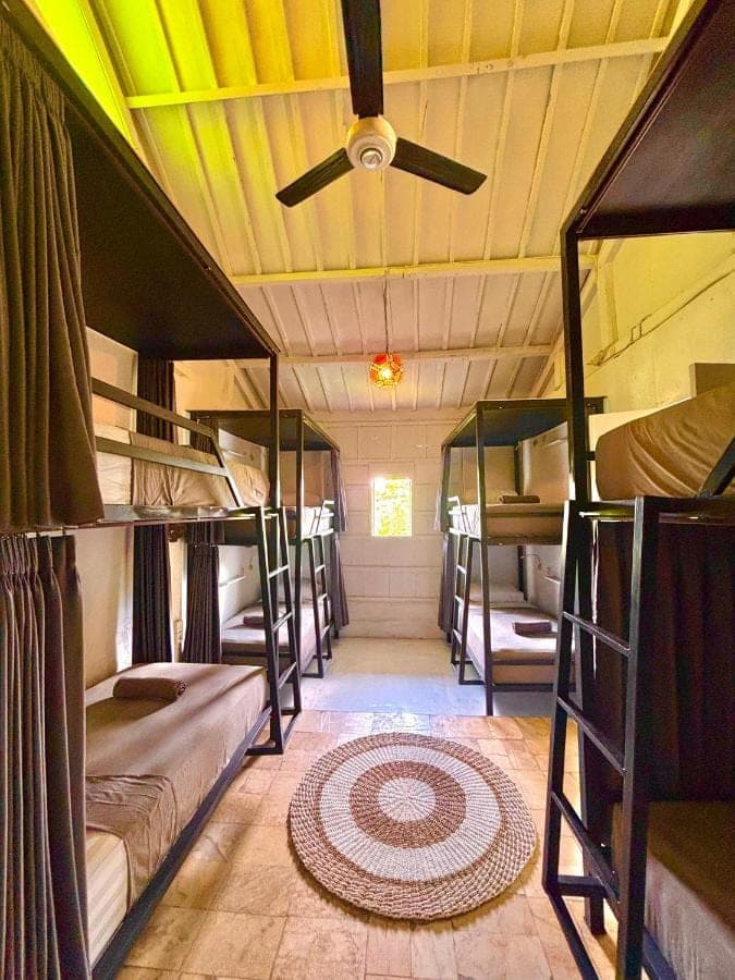 a room with several bunk beds and a ceiling fan at One More Wave Surf House Uluwatu in Uluwatu