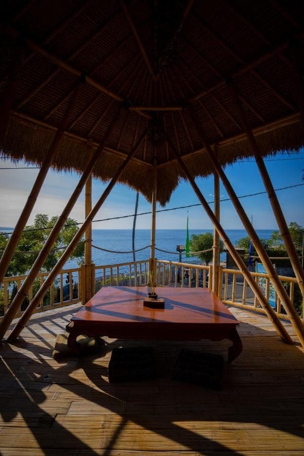 a table under a straw umbrella on a deck at Aroma De La Mer in Amed