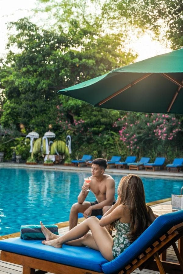 a man and a woman sitting on a beach chair next to a pool at Risata Bali Resort &amp; Spa in Kuta