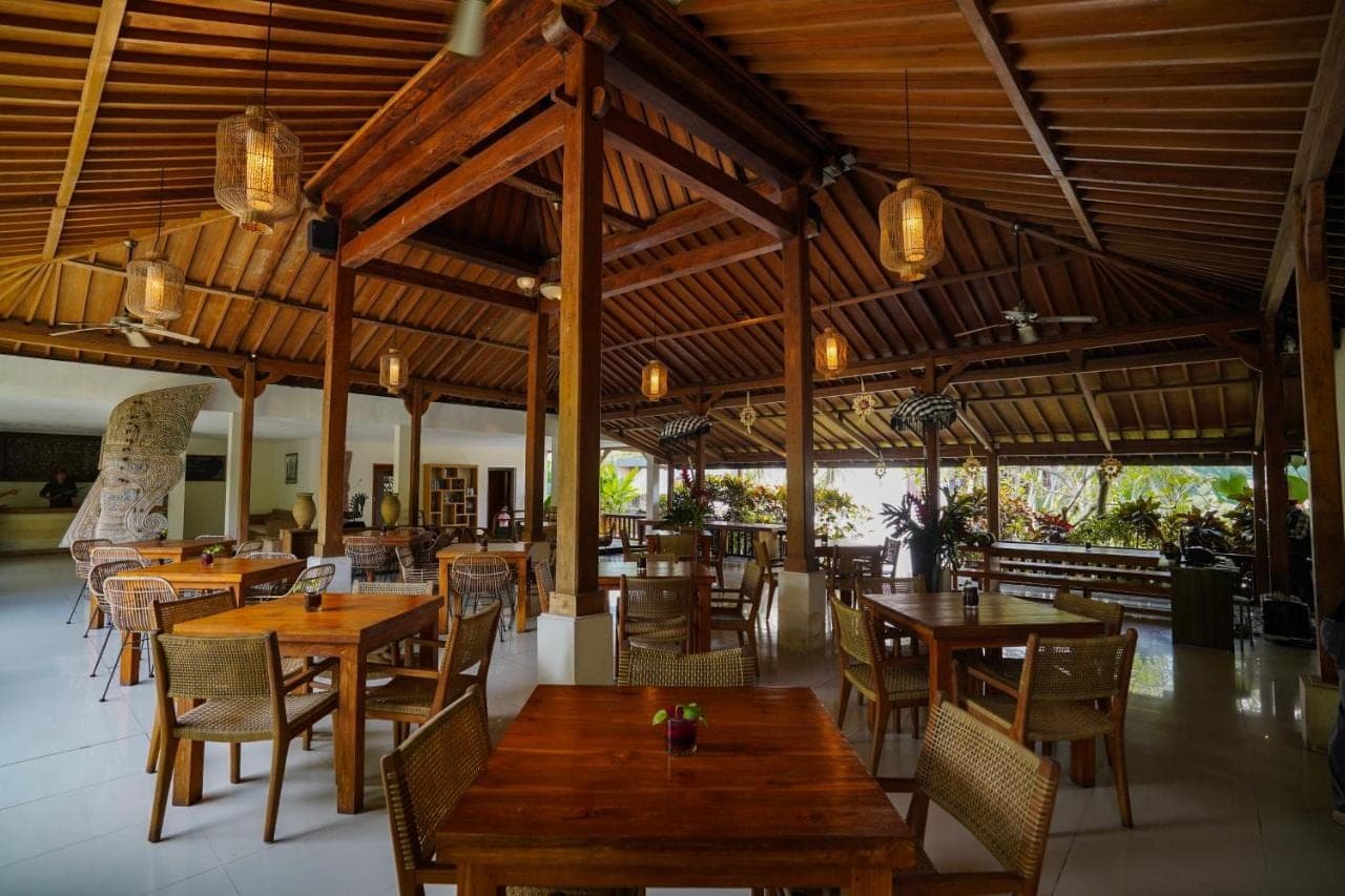 a restaurant with wooden tables and chairs in a building at Pertiwi Bisma 1 in Ubud
