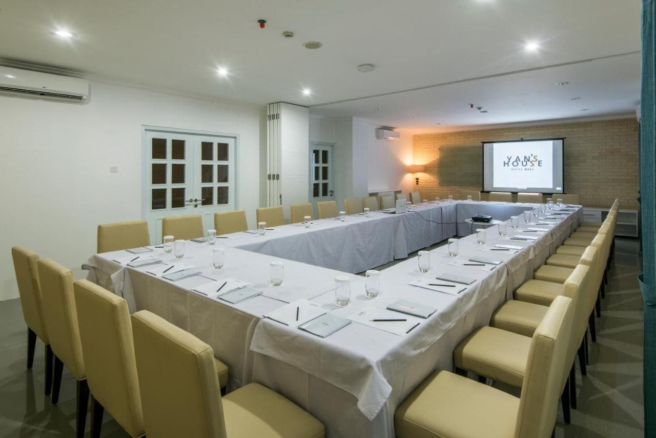 a long table in a room with chairs and a screen at Yan's House Hotel in Kuta