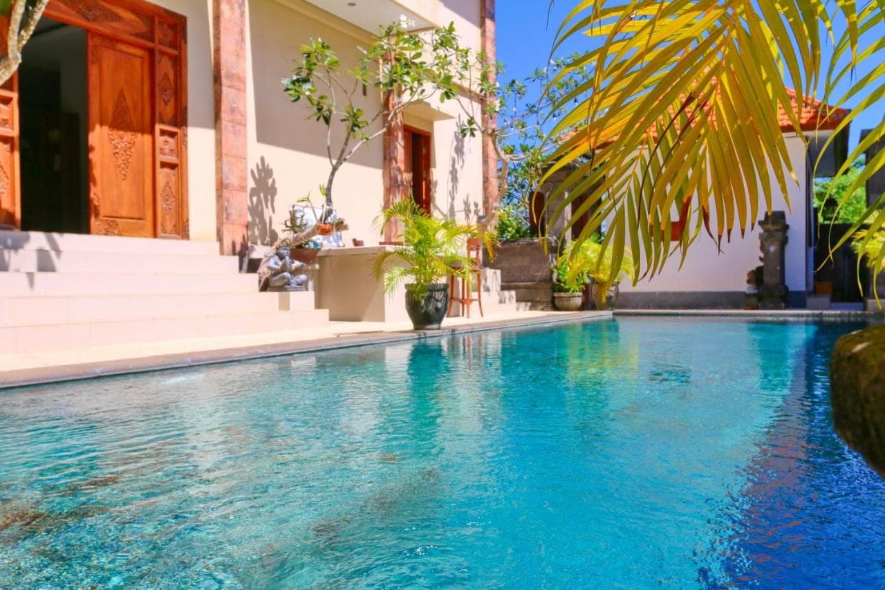 a swimming pool in front of a house with blue water at The Gong in Uluwatu