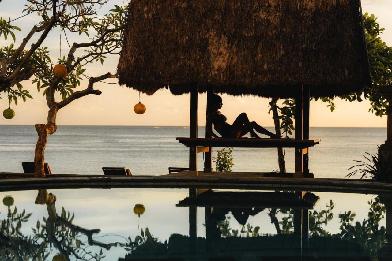 a woman sitting on a bench next to a swimming pool at Sunshine Bungalows in Amed