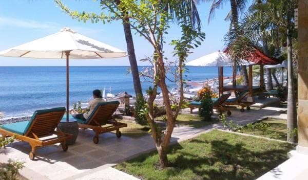 a man sitting in a chair under an umbrella at the beach at Apa Kabar Villas in Amed