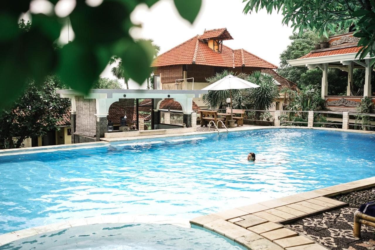 a person swimming in a large swimming pool at Amed Cafe &amp; Hotel Kebun Wayan in Amed