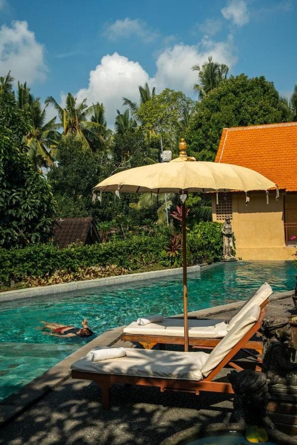 an umbrella and lounge chairs next to a swimming pool at Jati 3 Bungalows in Ubud