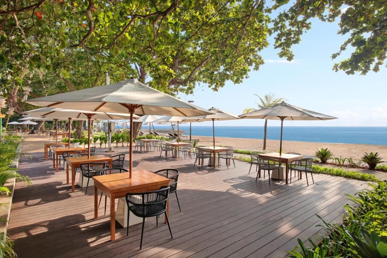 a deck with tables and umbrellas on the beach at eL Hotel &amp; Resort Bali Sanur in Sanur