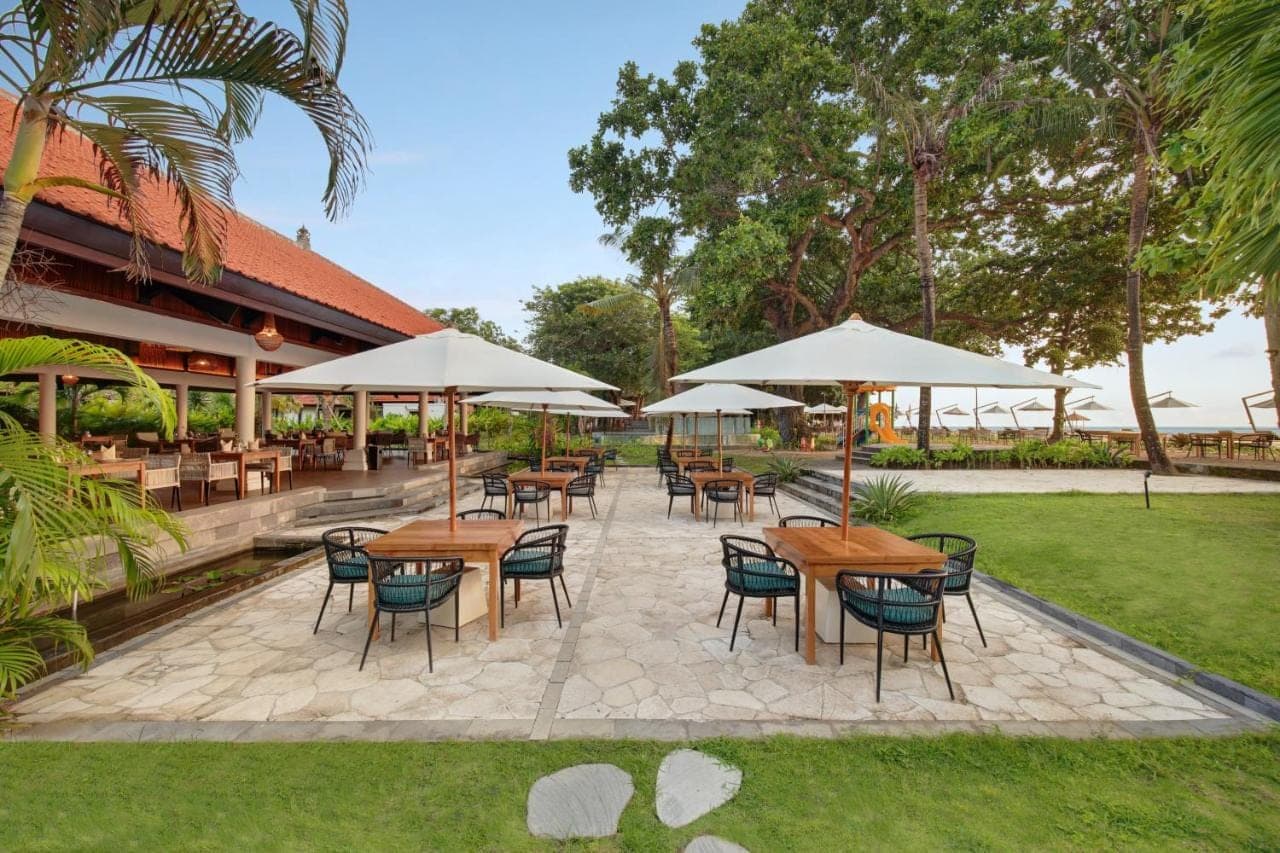 a patio with tables and chairs and umbrellas at eL Hotel &amp; Resort Bali Sanur in Sanur