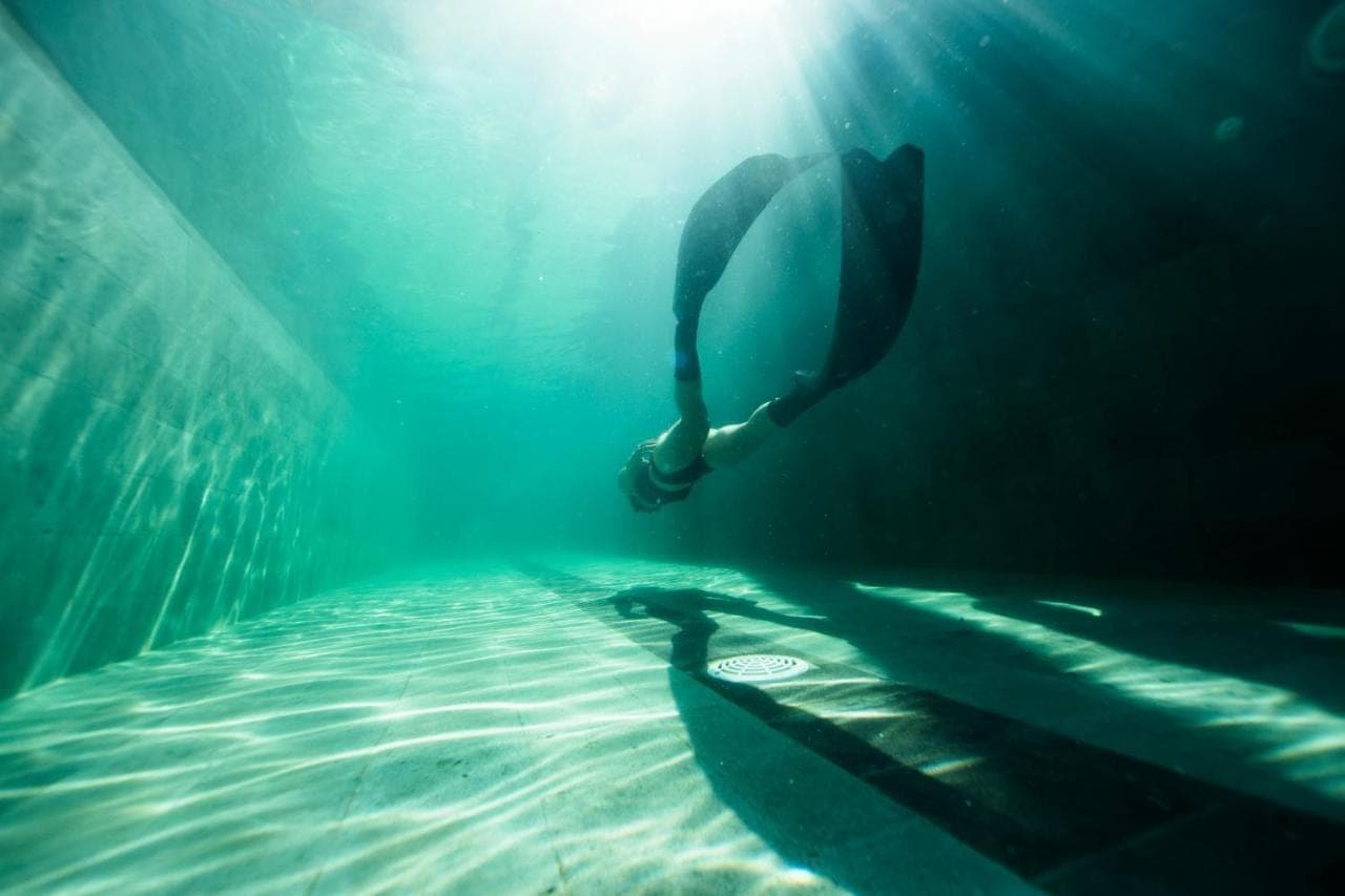 a person swimming in the water with a surfboard at Ocean Prana Village in Amed