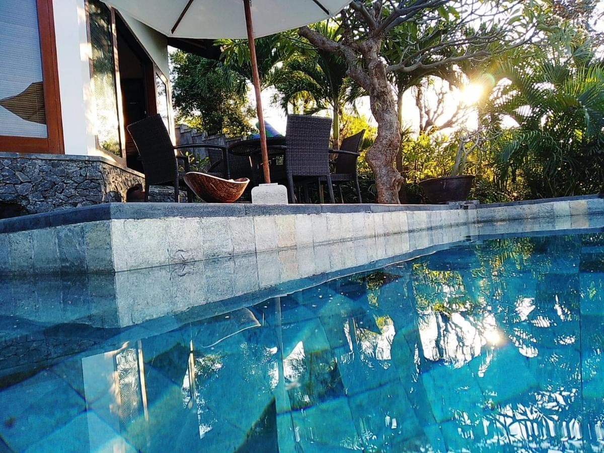 a swimming pool with an umbrella next to a house at Villa Mimpi Manis infinity pool&amp;180\u00b0Ocean view in Amed
