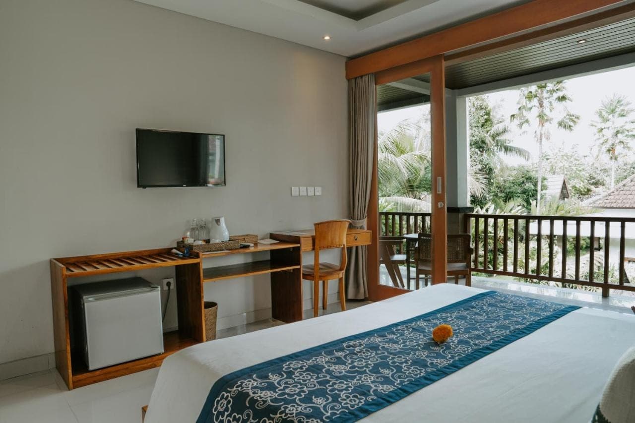 a bedroom with a bed and a desk and a balcony at The Umari in Ubud