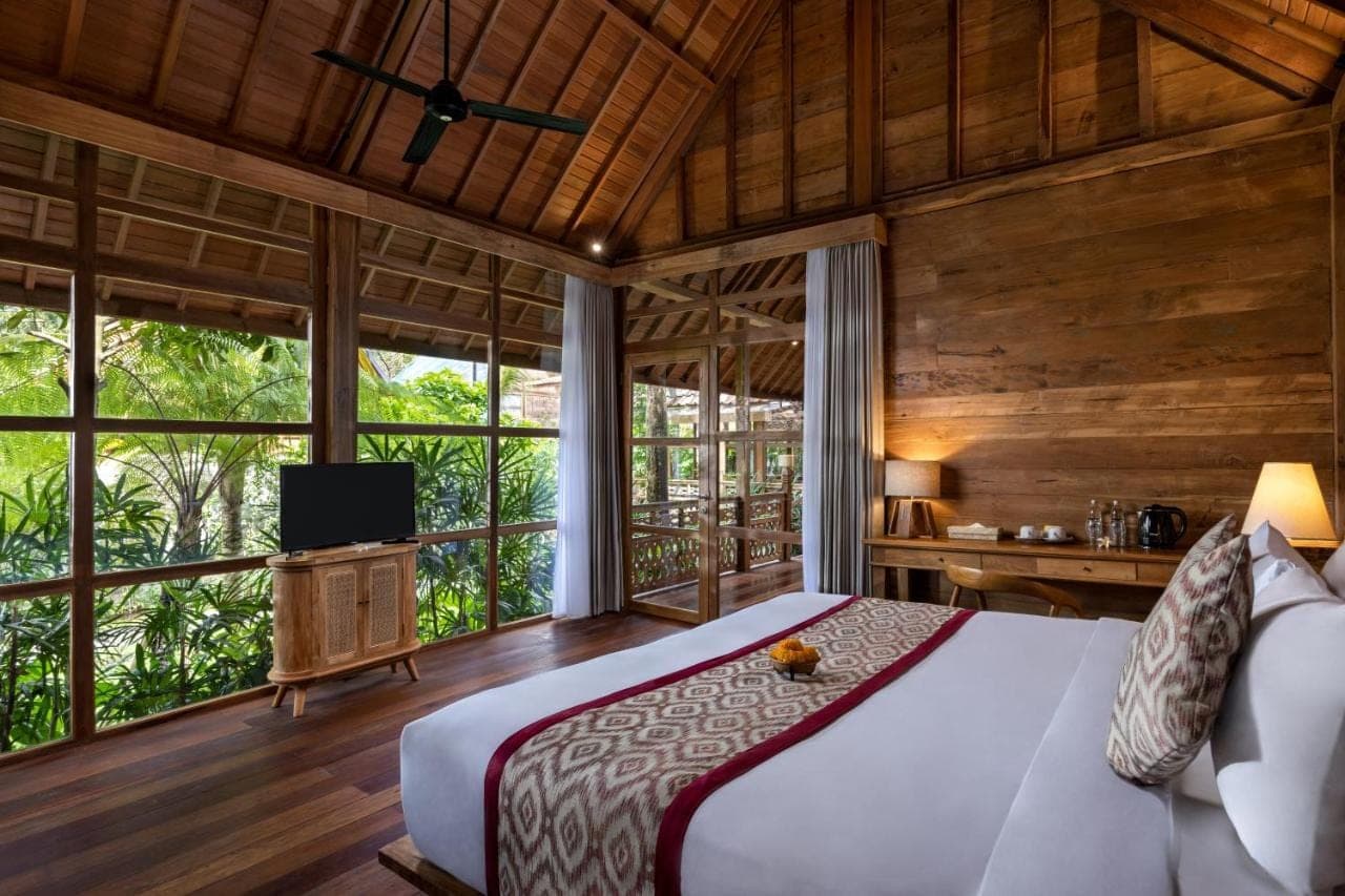a bedroom with a bed and a tv and windows at RUMAH KAYU RESORT in Ubud