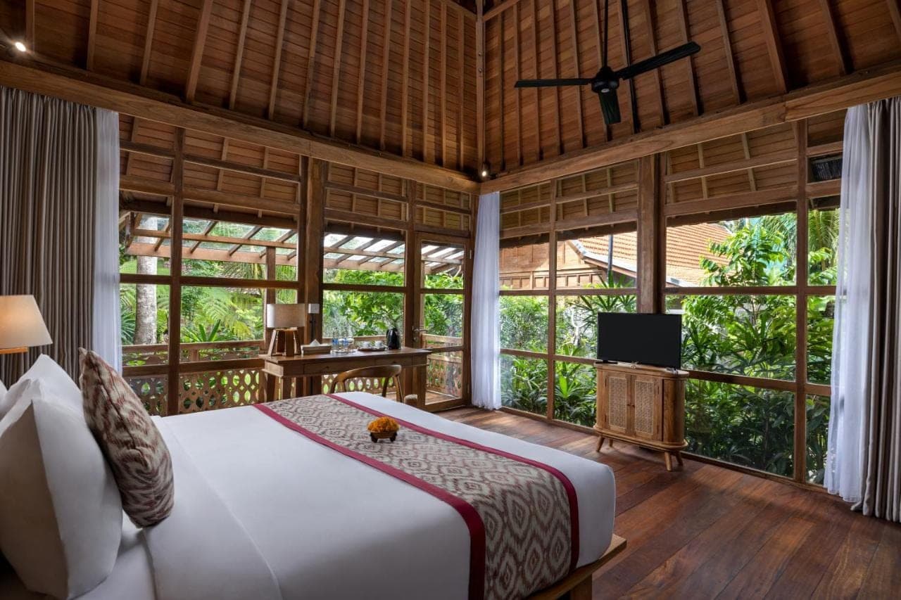 a bedroom with a bed in a room with large windows at RUMAH KAYU RESORT in Ubud