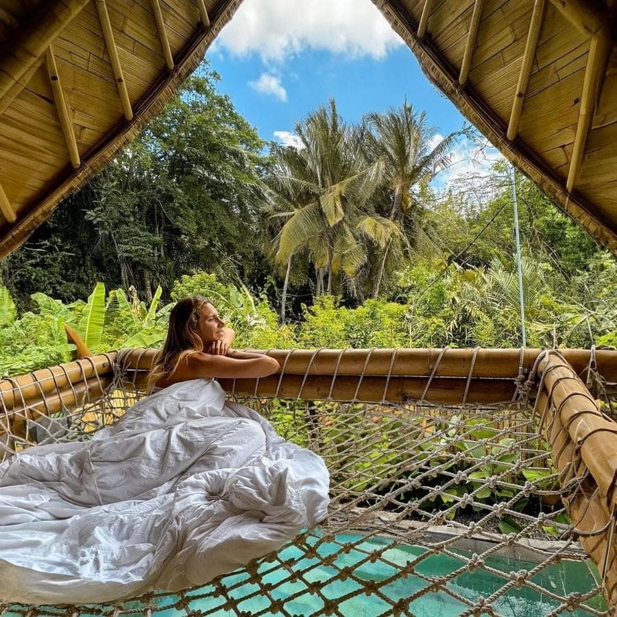 a woman laying on a suspension bridge over a river at Bamboo House - Ecobreeze in Sidemen