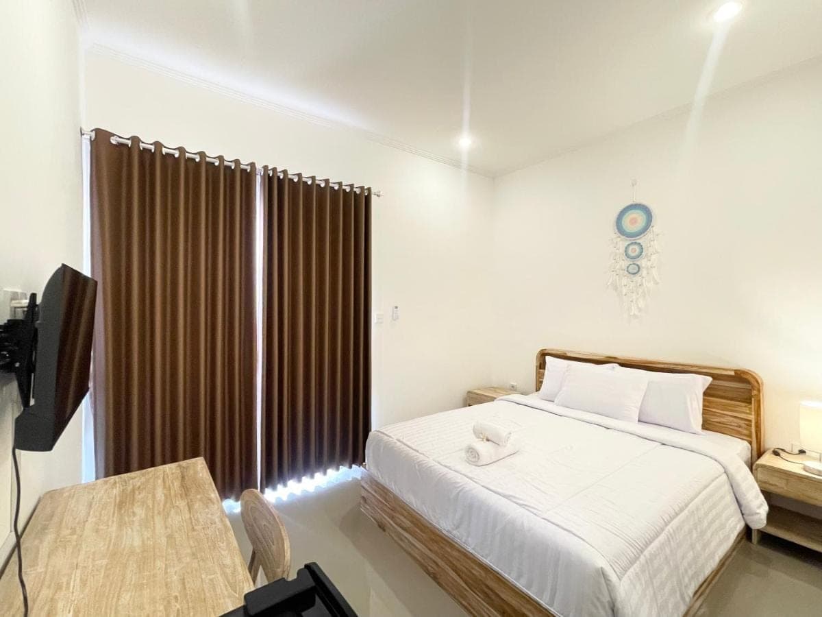a bedroom with a bed and a desk and a television at Umah Wayan Sanur in Sanur