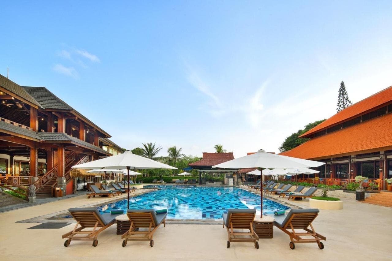 a pool with chairs and umbrellas next to a building at Grand Istana Rama Hotel in Kuta