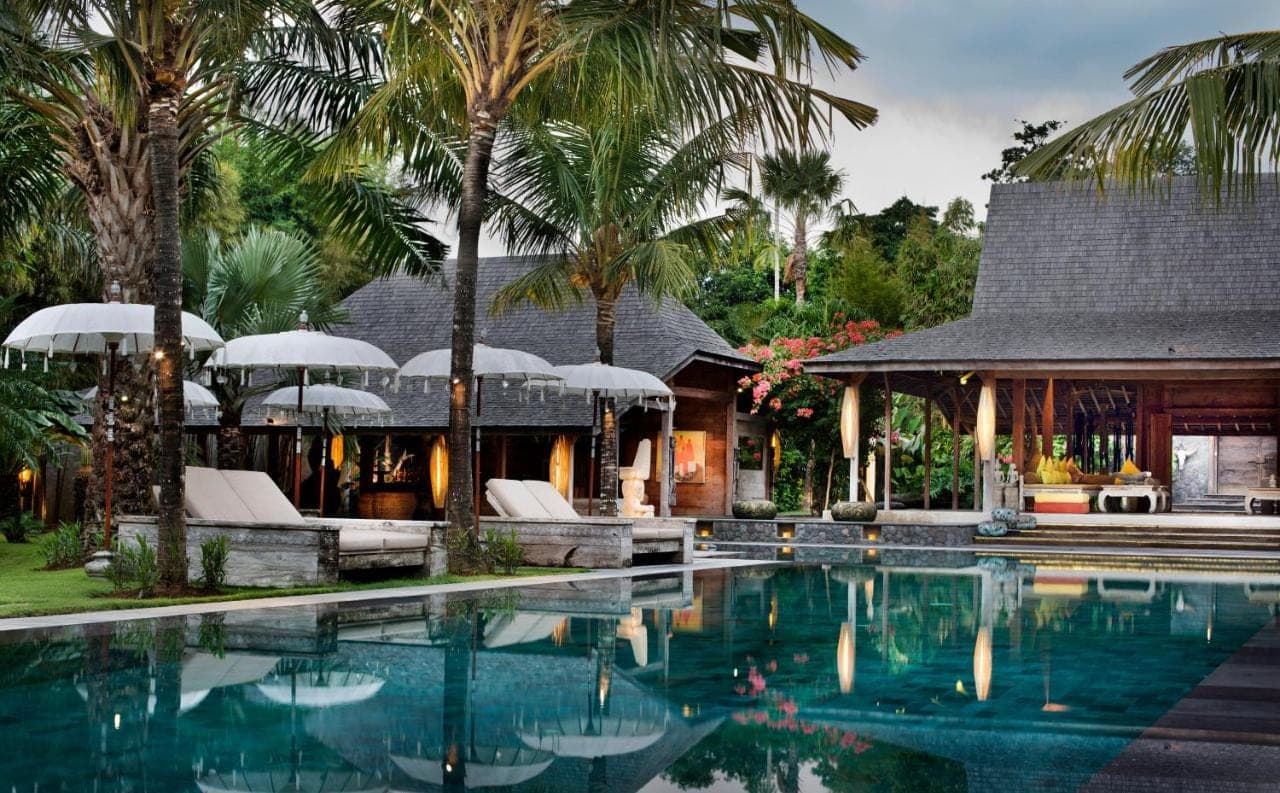 a swimming pool in front of a house with palm trees at Blue Karma Village in Seminyak