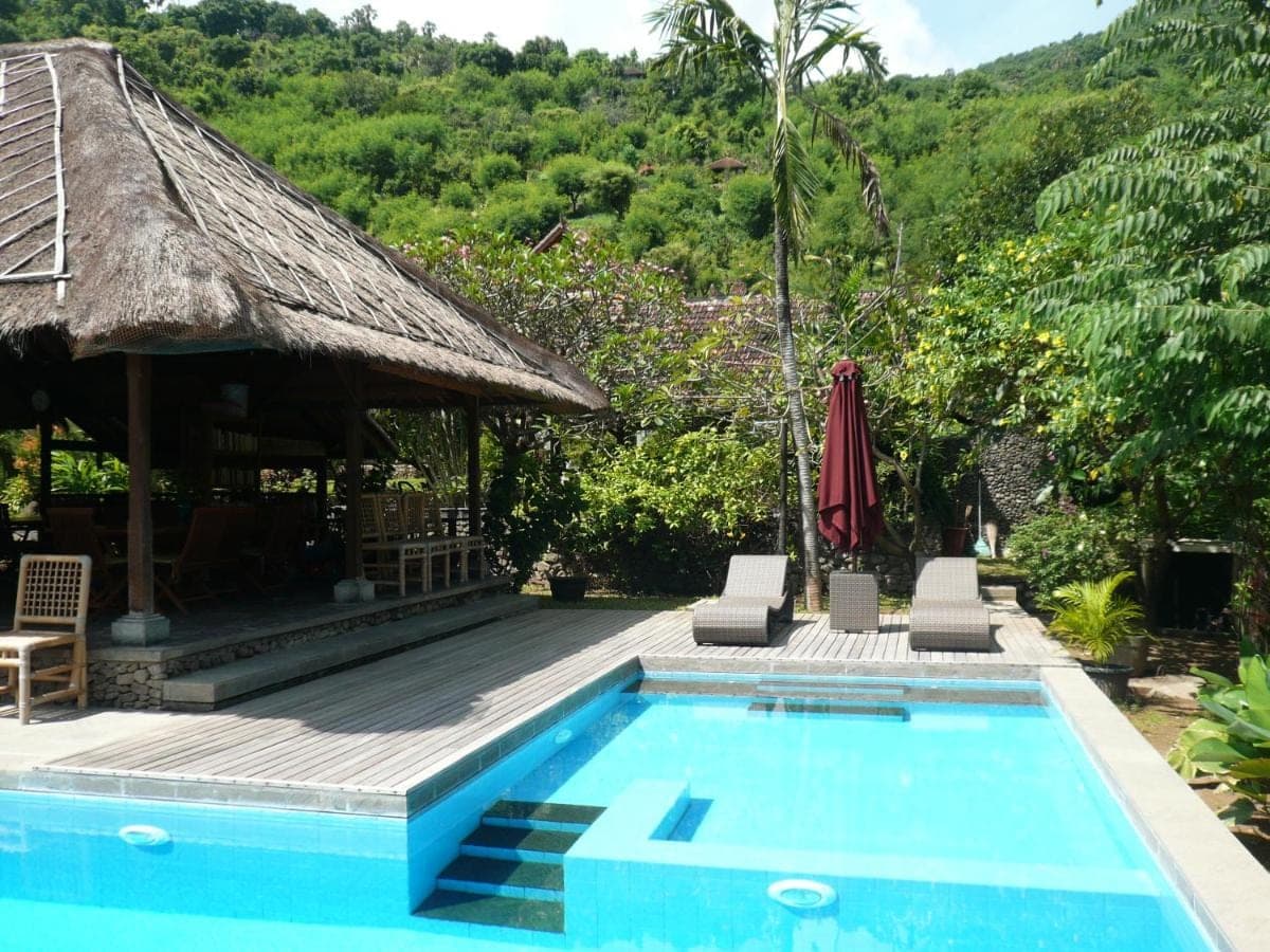 a swimming pool next to a house with a hut at Le Jardin in Amed
