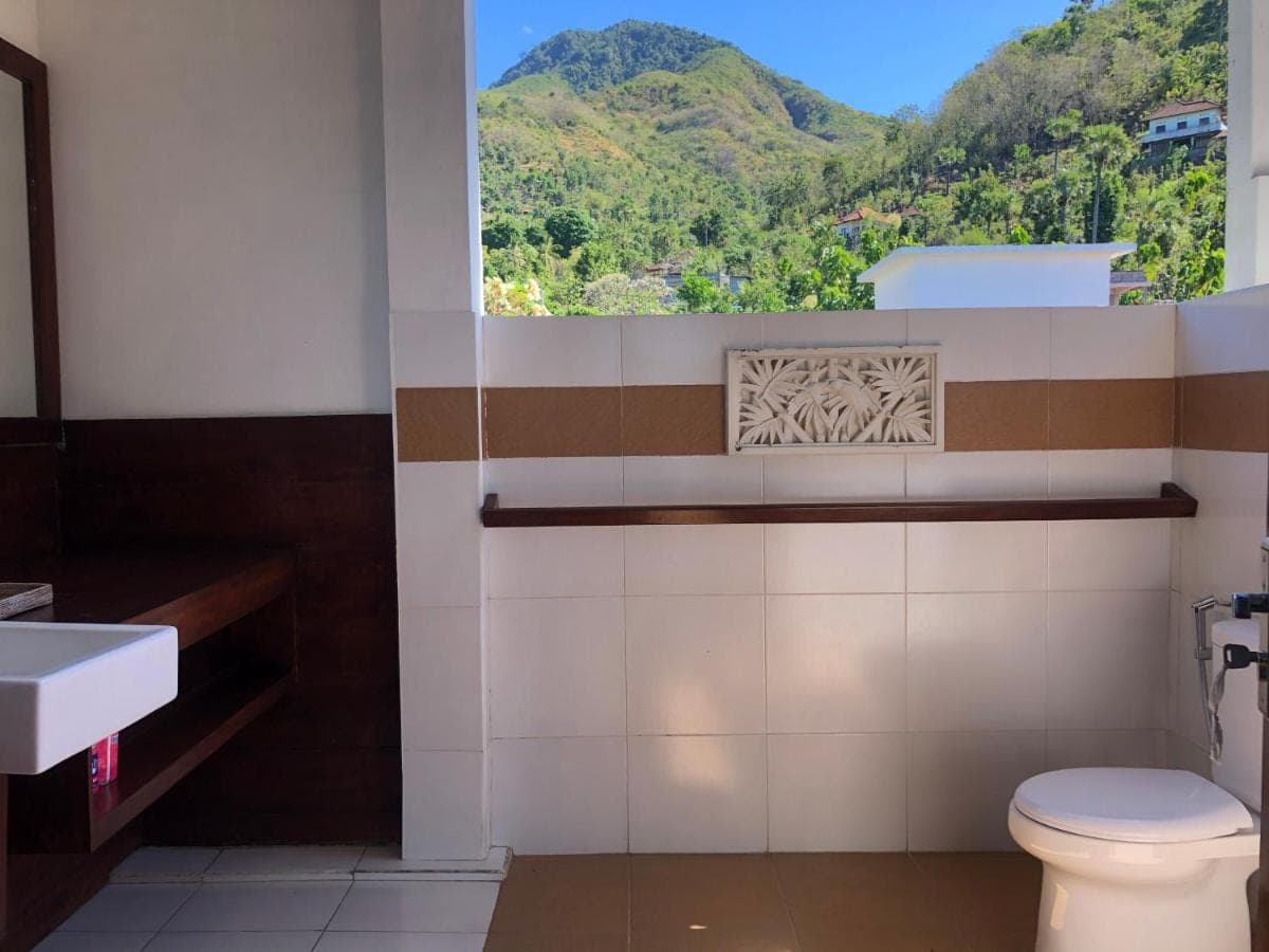 a bathroom with a toilet and a window with mountains at Meditasi Bungalows &amp; Villas in Amed