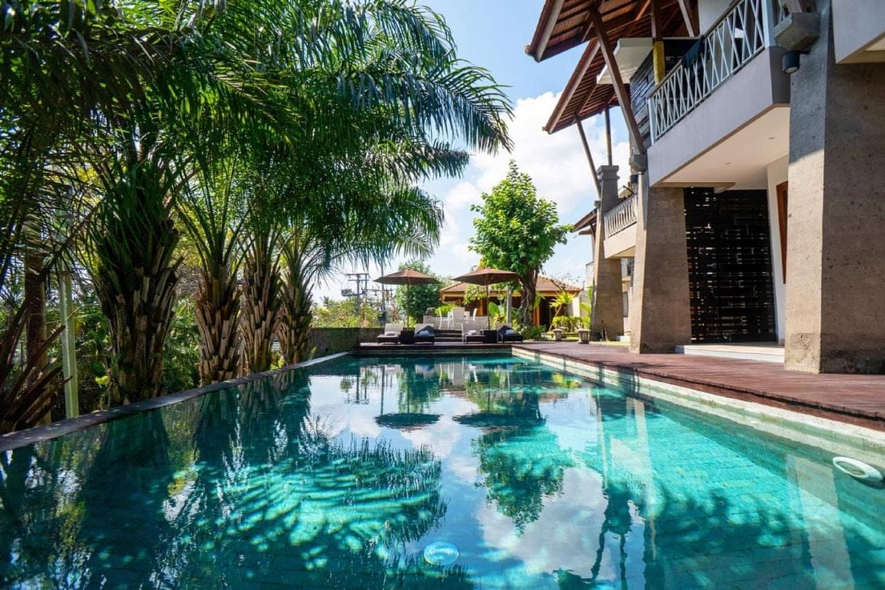 a swimming pool in front of a house with palm trees at djabu Echo Beach Hotel in Canggu