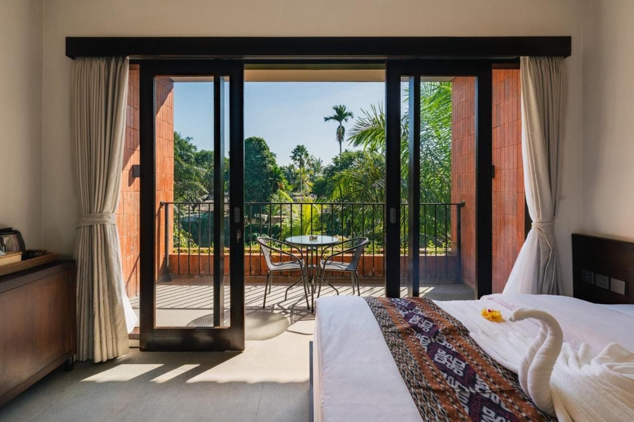 a bedroom with a bed and a balcony with a table at Kuma House in Ubud
