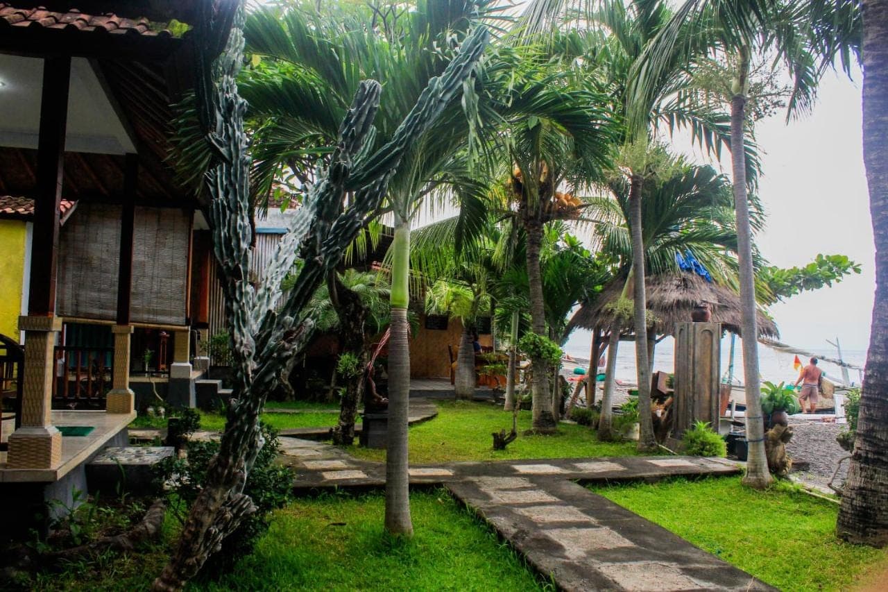 a resort with palm trees in front of a building at COCONUT BEACH BUNGALOWs &amp; WARUNG 2 in Amed