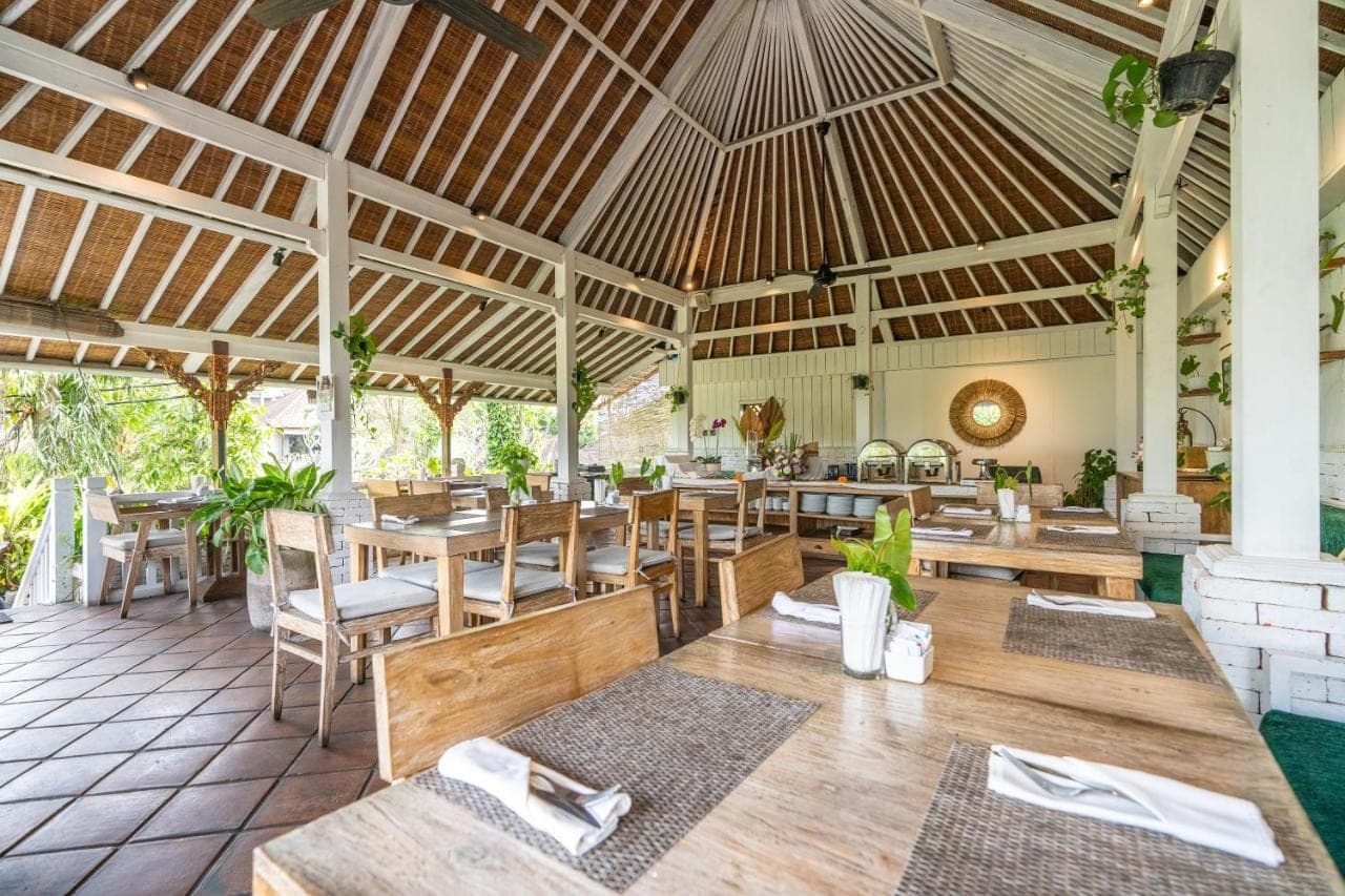 an empty restaurant with wooden tables and chairs at Bliss Ubud Spa Resort in Ubud