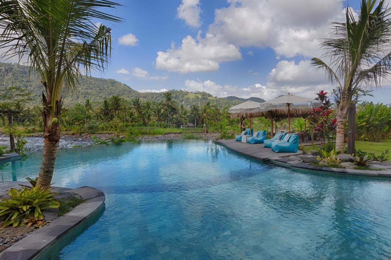 a swimming pool with blue chairs and palm trees at Natya River Sidemen in Sidemen