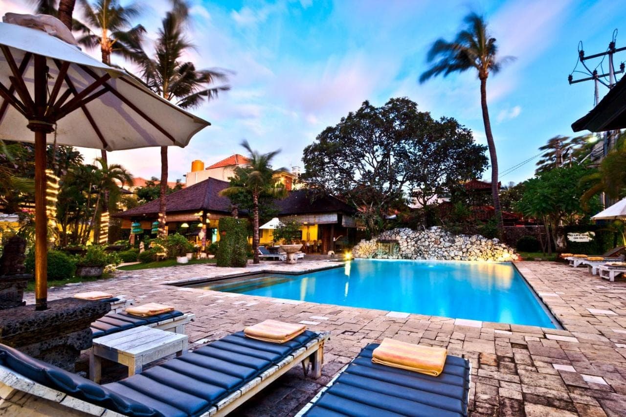 a swimming pool with lounge chairs and an umbrella at Palm Garden Hotel in Sanur