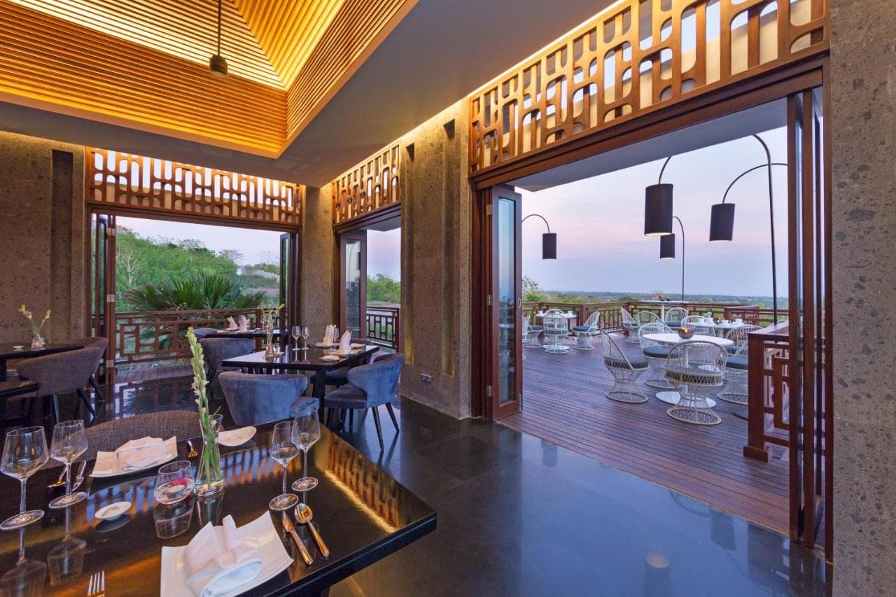a restaurant with tables and chairs and large windows at Prasana Villas Uluwatu in Uluwatu